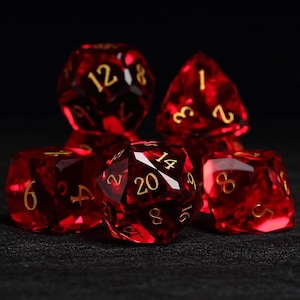May include: A set of red polyhedral dice with gold numbers. The dice are made of a clear material with a red tint. The dice are arranged in a pile, with the 20-sided die on top.