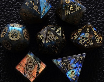 Może przedstawiać: Zestaw siedmiu iryzujących niebieskich i złotych kości z kamieni szlachetnych z symbolami niebieskimi i astrologicznymi. Kości są fasetowane i mają unikalny, mistyczny design.