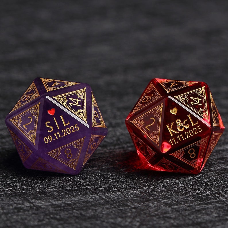 May include: Two personalized D20 dice, one purple and one red, with gold filigree and engraved names and dates. The purple die has "S|L" and "09.11.2025", while the red die has "K&L" and "11.11.2025". Each die features a heart symbol.