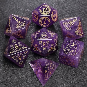 Pode incluir: Conjunto de sete dados de ametista roxa com desenhos de gato e lua dourados. Os dados são numerados de 4 a 20.
