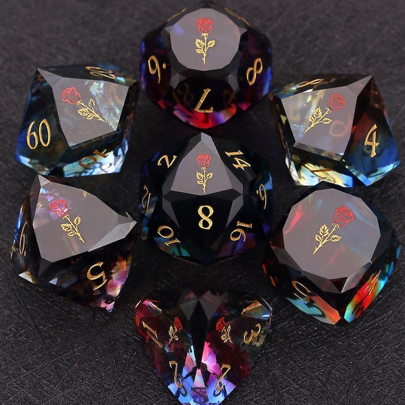 Op de afbeelding: Set van zeven polyhedrale dobbelstenen met een donkere, iriserende afwerking. Elke dobbelsteen heeft gouden cijfers en een rood rozenembleem. De dobbelstenen zijn ontworpen voor tabletop-rollenspellen en hebben verschillende geometrische vormen.