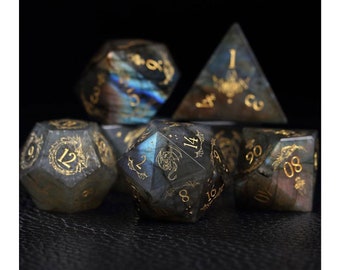May include: Set of seven black and gold gemstone dice with a dragon design. The dice are made of labradorite and have a metallic gold finish.