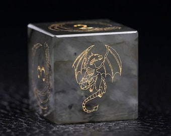 May include: A grey, translucent dice with a gold dragon design etched on one side. The dragon is facing right with its wings spread out. The dice is made of natural stone.