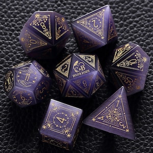 May include: Set of seven purple gemstone dice with gold-colored numbering and celestial designs. The dice include a D4, D6, D8, D10, D12, D20, and a D%. The D20 die has the initials "C&B" and the date "20.09.2025".