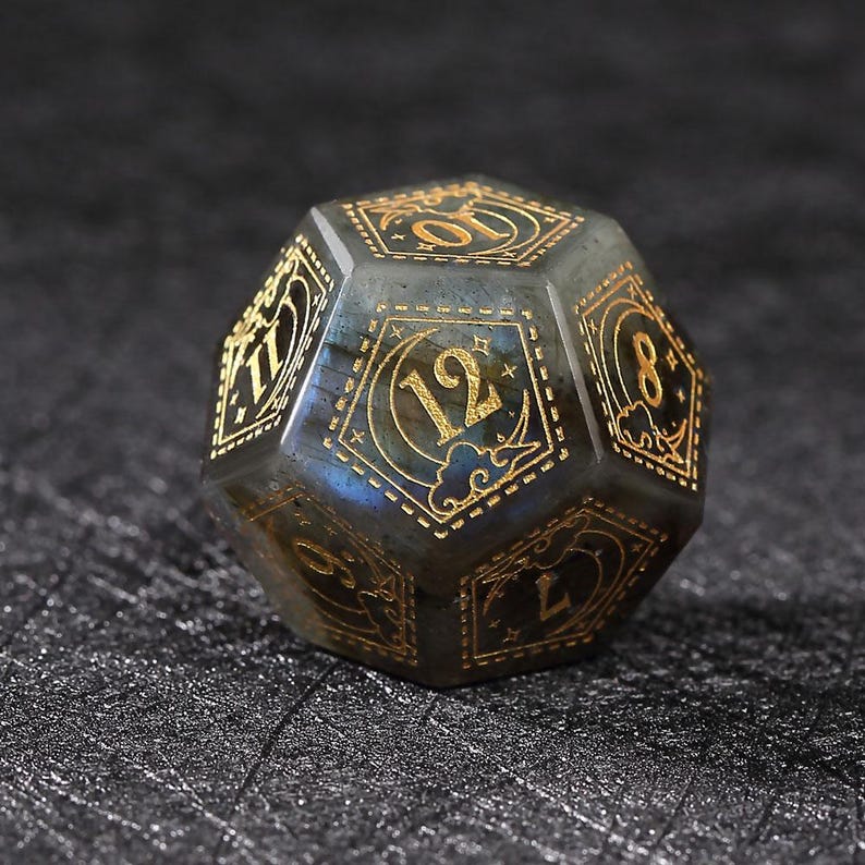 May include: A multi-sided, gemstone die with gold-colored numerals and decorative accents. The die is a mix of gray and blue with a polished finish. The numbers are in a classic font, and the die is likely used for tabletop gaming.