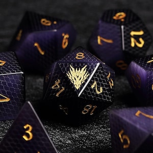 May include: Set of polyhedral dice in shades of purple and black with gold numbering. The dice have a textured, scale-like pattern. One die features a gold dragon emblem. Ideal for tabletop gaming.