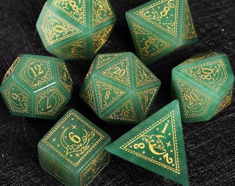 Op de afbeelding: Set van zeven groene polyhedrale dobbelstenen met goudkleurige cijfers en decoratieve ontwerpen. De dobbelstenen, waaronder d4, d6, d8, d10, d12, d20 en een percentieldobbelsteen, liggen op een donkere ondergrond. Elke dobbelsteen heeft gouden details.