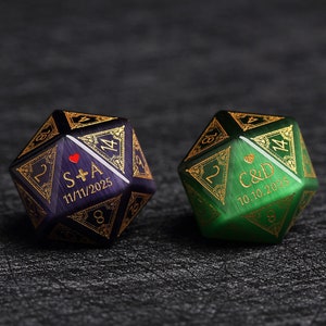 May include: Two dodecahedron dice, one purple and one green, with gold-colored filigree and engraved text. The purple die has "S+A" and "11/11/2025". The green die has "C&D" and "10.10.2025".