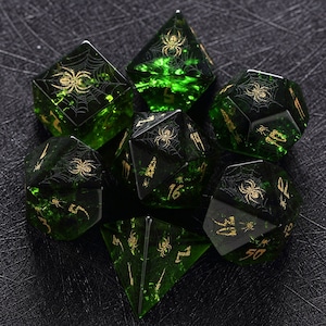以下が含まれることがあります： クモとクモの巣のデザインが施された緑と金のサイコロ7個セット。サイコロは透明な緑色のガラス製で、金色のアクセントが施され、各面にクモとクモの巣のデザインが施されています。