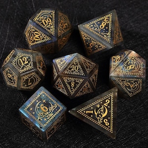 May include: Set of seven polyhedral dice with gold-colored numbers and celestial designs. The dice are a mix of blue, gray, and brown, with a translucent appearance. The dice are for tabletop games.