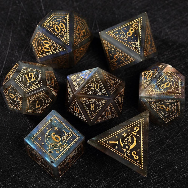 May include: Set of seven polyhedral dice with gold-colored numbers and celestial designs. The dice are a mix of blue, gray, and brown, with a translucent appearance. The dice are for tabletop games.