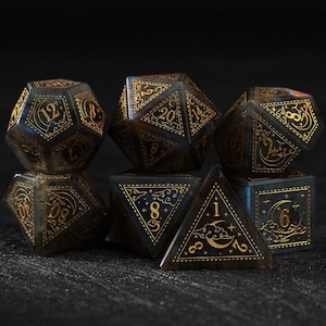 May include: Set of seven polyhedral dice in various shapes, featuring a dark blue and gold color scheme. Each die has gold numbering and decorative celestial designs, perfect for tabletop gaming.