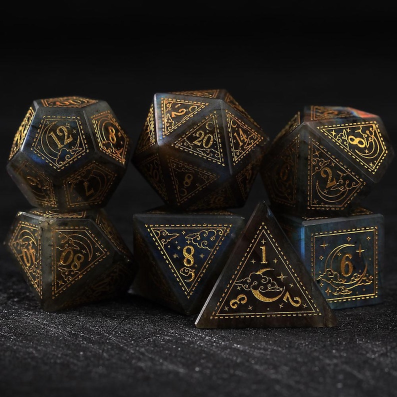 May include: Set of seven polyhedral dice in various shapes, featuring a dark blue and gold color scheme. Each die has gold numbering and decorative celestial designs, perfect for tabletop gaming.