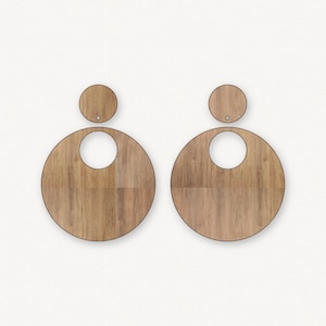 以下が含まれることがあります： 丸い形をした木製のイヤリングのペア。中央に小さな円がくり抜かれています。イヤリングには自然な木目模様があります。