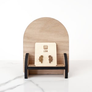 May include: A pair of wooden rose stud earrings displayed on a wooden stand with a small card that says "LOOK" and a logo of a stylized eye.