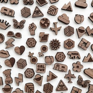 Image showing an example of an array of laser cut earring studs. Studs are cut and engraved in walnut wood. Shapes include airplane, earth, world, geometric shapes, black lives matter, lightning, woman figure, mountain, daisy, flower, butterfly, etc.