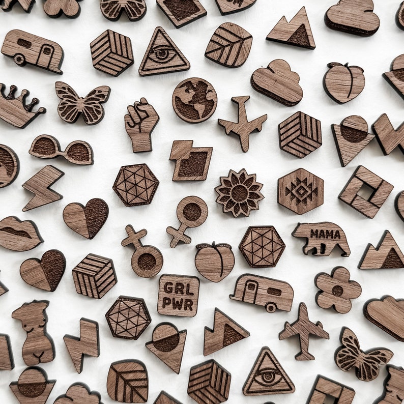 Image showing an example of an array of laser cut earring studs. Studs are cut and engraved in walnut wood. Shapes include airplane, earth, world, geometric shapes, black lives matter, lightning, woman figure, mountain, daisy, flower, butterfly, etc.