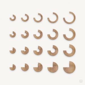 Puede incluir: Un conjunto de 15 círculos de madera, cada uno con un tamaño diferente y una parte cortada, creando una forma de media luna. Los círculos están dispuestos en una cuadrícula, con los círculos más grandes en la parte superior y los círculos más pequeños en la parte inferior.