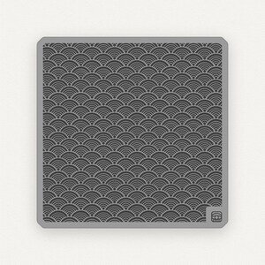May include: A gray square tile with a repeating pattern of black and white overlapping semi-circles. The tile has a slightly raised border.
