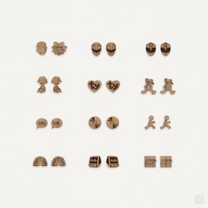 Puede incluir: Una colección de pendientes de madera con diversas formas y diseños. Los pendientes incluyen personajes de dibujos animados, corazones con el texto "ty", osos de peluche, bocadillos con el texto "LOL", CDs, figuras corriendo, abanicos, ordenadores retro con el texto "hello" y diseños cuadrados.