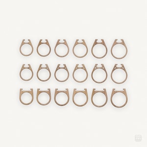Könnte beinhalten: Ein Satz von 16 Holzringen, jeder mit einem einzigartigen Design. Die Ringe sind in vier Reihen zu vier angeordnet, wobei jede Reihe ein anderes Design aufweist. Die Ringe sind alle aus Naturholz gefertigt und haben eine hellbraune Farbe.
