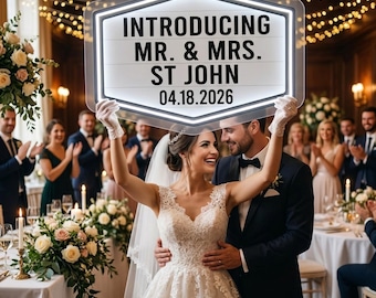 Puede incluir: Una pareja de recién casados sostiene un letrero luminoso en su boda. El letrero dice "INTRODUCING MR. & MRS. ST JOHN 04.18.2026". El letrero es blanco con un borde negro. Los novios están rodeados de invitados en la recepción.