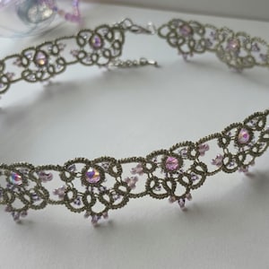 May include: A silver-toned, open-work choker necklace with a delicate floral design. The necklace is adorned with iridescent pink crystals and smaller pink beads, creating a sparkling effect. The clasp is visible at the back.
