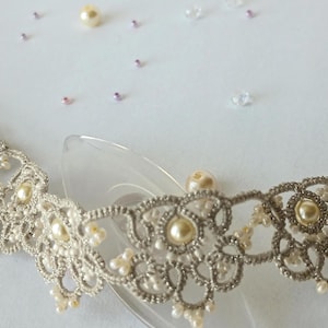 May include: A delicate, silver-colored lace collar with pearl accents. The intricate design features floral patterns and small, round pearls. Scattered pearls and beads are visible in the background, suggesting a bridal or formal theme.