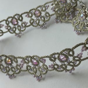 May include: A silver-toned choker necklace with a delicate, openwork design. The necklace is adorned with iridescent pink crystals and smaller pink beads. The intricate lace-like pattern creates a romantic and elegant aesthetic, suitable for special occasions.