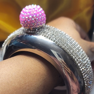 May include: A silver bracelet with a pink rhinestone top. The bracelet is decorated with clear rhinestones.