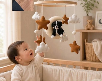 Peut inclure: Un mobile de chambre d'enfant suspendu avec un cadre circulaire en bois et des éléments en feutrine incluant des nuages blancs, des étoiles marron, un croissant de lune crème et un petit chien noir et blanc rappelant la photo insérée.
