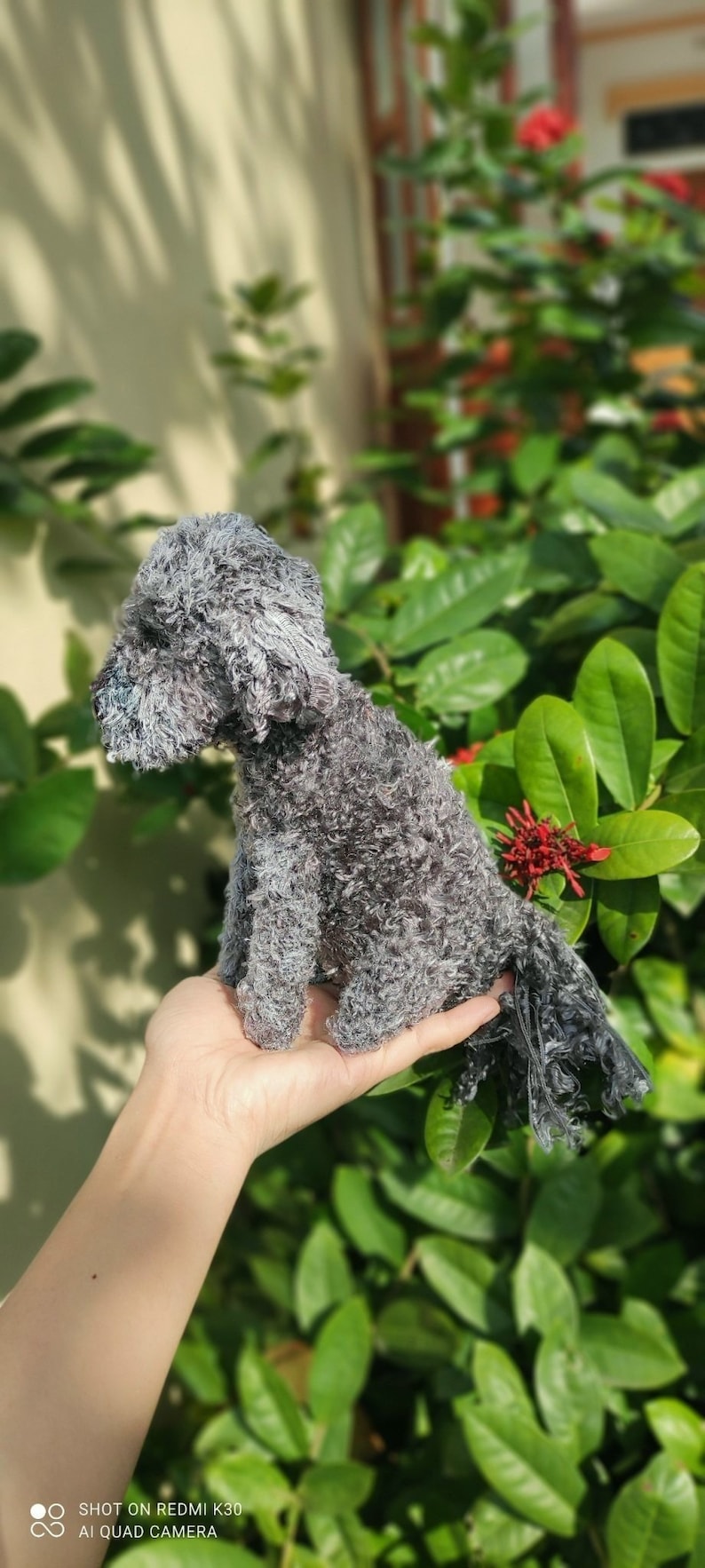 May include: A small, gray, fluffy dog toy is being held in a person's hand. The dog toy has a long, fluffy tail.