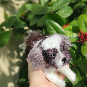 May include: A small, crocheted, brown and white dog toy. The toy is being held in a person's hand.