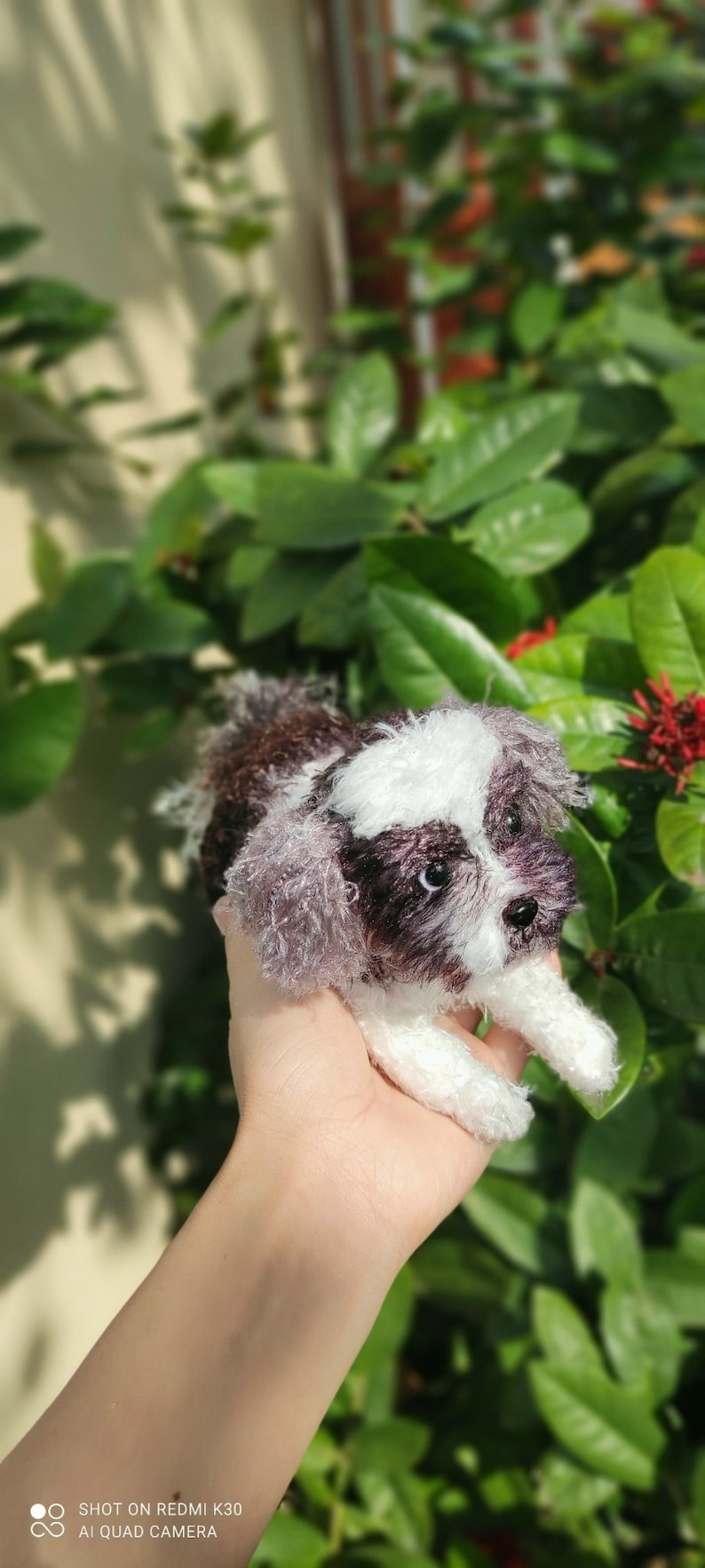 May include: A small, crocheted, brown and white dog toy. The toy is being held in a person's hand.