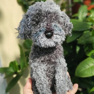 May include: A small gray fluffy dog toy sitting in a person's hand. The toy has a black nose and is made of soft, fuzzy material.