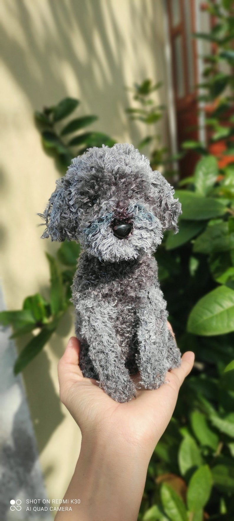 May include: A small gray fluffy dog toy sitting in a person's hand. The toy has a black nose and is made of soft, fuzzy material.
