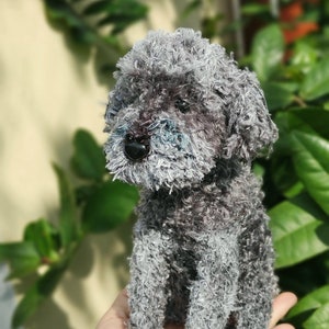 May include: A gray and white plush toy poodle with a fluffy texture. The toy is sitting on a person's hand.