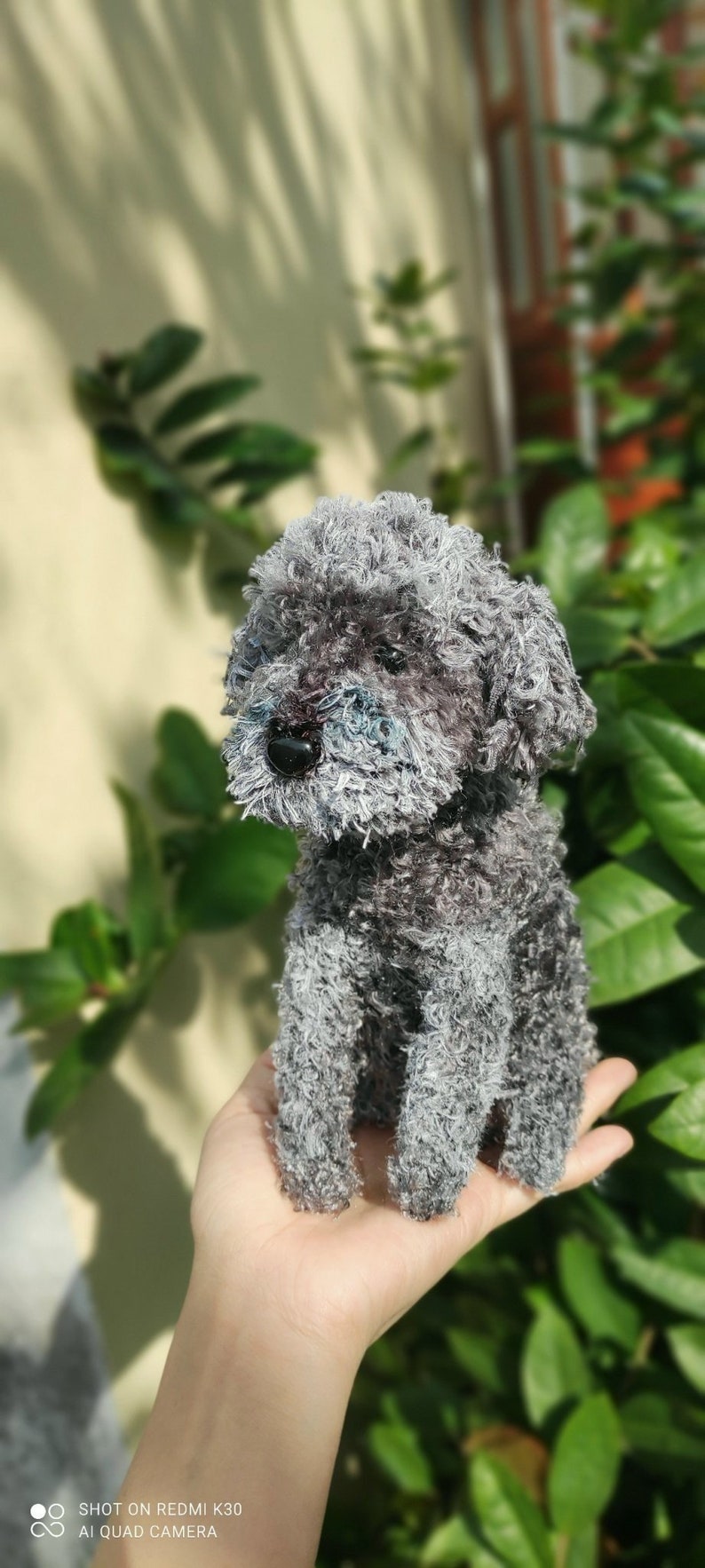 May include: A gray and white plush toy poodle with a fluffy texture. The toy is sitting on a person's hand.