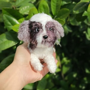 May include: A small, white and black crocheted dog toy. The dog is sitting up with its paws in the air. The toy is being held in a person's hand.