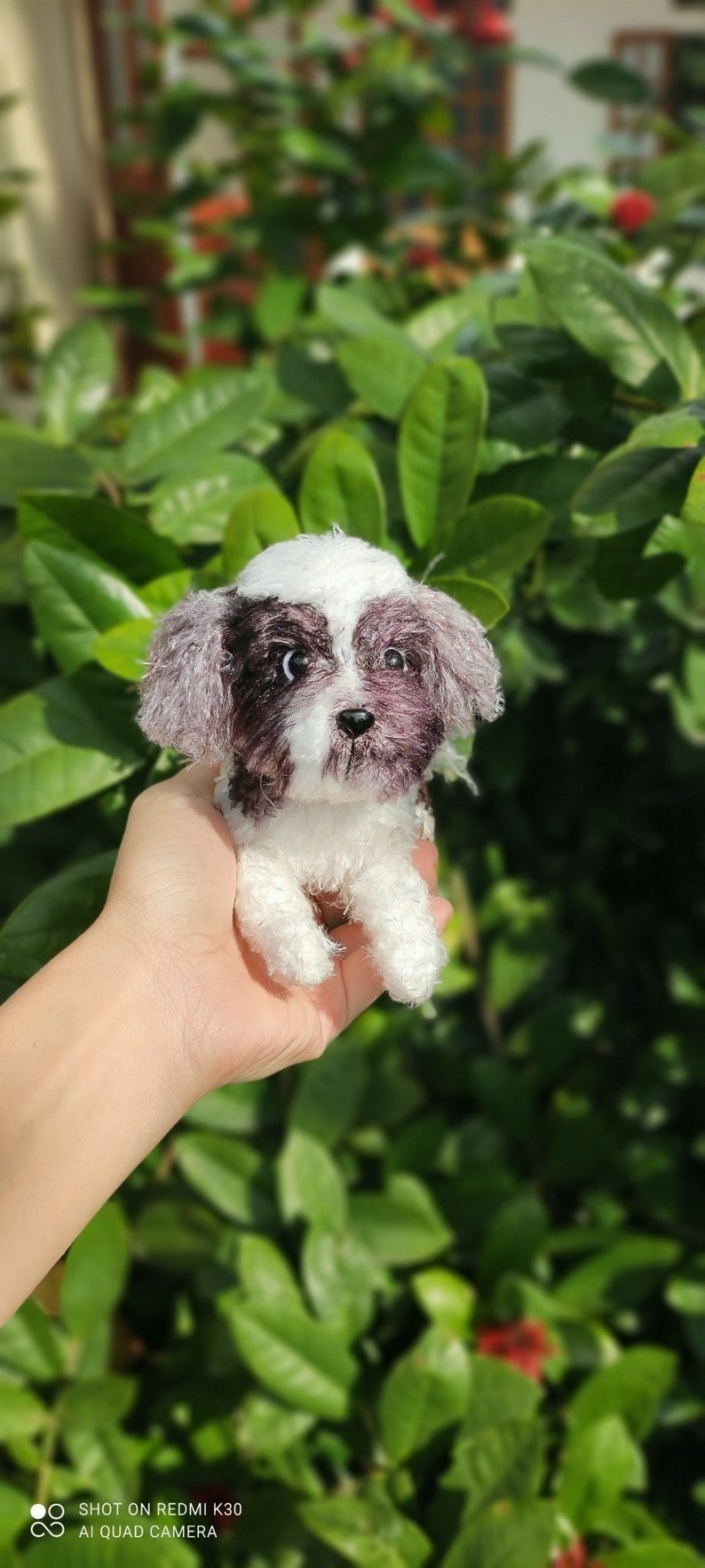 May include: A small, white and black crocheted dog toy. The dog is sitting up with its paws in the air. The toy is being held in a person's hand.