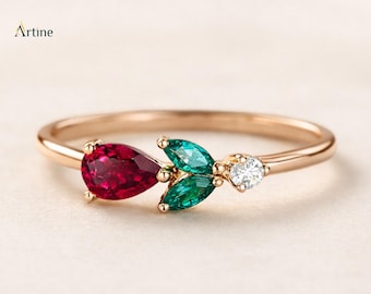 Op de afbeelding: Een roségouden ring met een peervormige rode edelsteen, twee marquise-geslepen groene edelstenen en een kleine ronde witte edelsteen in een cluster. De merknaam Artine staat in de linkerbovenhoek van de afbeelding gedrukt.