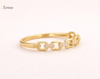May include: A gold ring featuring a chain-link design with small, clear, round-cut stones embedded in alternating links. The band is polished gold, and the word Artine is printed in the upper left corner of the image.