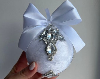 Puede incluir: Un adorno navideño de terciopelo blanco con un gran lazo de satén blanco y un adorno de cristal.