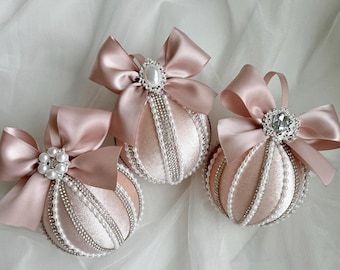 May include: Three blush pink velvet Christmas ornaments with pearl and rhinestone embellishments. Each ornament is adorned with a blush pink satin bow.