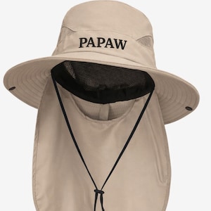 May include: Beige sun hat with a wide brim and a neck flap for sun protection. The hat features the word "PAPAW" embroidered in black on the front. It has a mesh section for ventilation and an adjustable chin strap.