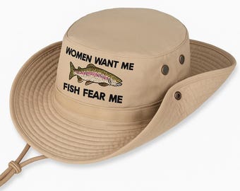 May include: Tan fishing hat with a wide brim and a chin strap. The hat features the text "WOMEN WANT ME FISH FEAR ME" with an embroidered fish graphic. The hat has metal eyelets and a drawstring for adjustment.