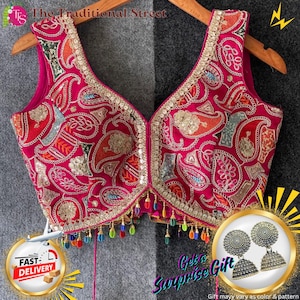 Pode incluir: Um top sem mangas, magenta, com bordados paisley intrincados em ouro, laranja e vermelho. O decote em V é adornado com lantejoulas douradas e borlas de contas coloridas. O texto "The Traditional Street" é visível.
