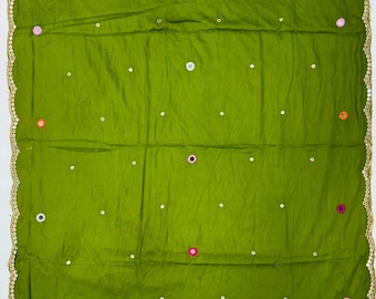 Può includere: Una sciarpa rettangolare in tessuto verde oliva con un bordo dorato smerlato. La superficie è decorata con un motivo ripetitivo di piccoli specchi circolari e minuscole borchie metalliche nei colori rosa, arancione e bianco sul tessuto.