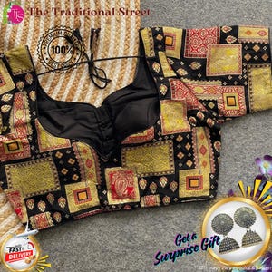 Pode incluir: Uma blusa preta com um padrão decorativo em quadrados dourados, vermelhos e amarelos. A blusa tem um decote em V profundo e é exibida com um par de brincos de prata. O texto "The Traditional Street" e "Get a Surprise Gift" são visíveis.