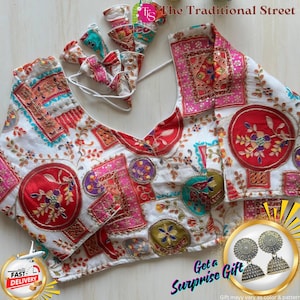 Pode incluir: Blusa branca com um design de patchwork colorido com detalhes em vermelho, rosa e azul. A blusa tem decote em V e laços decorativos. O texto "The Traditional Street" é visível. Inclui um presente surpresa.